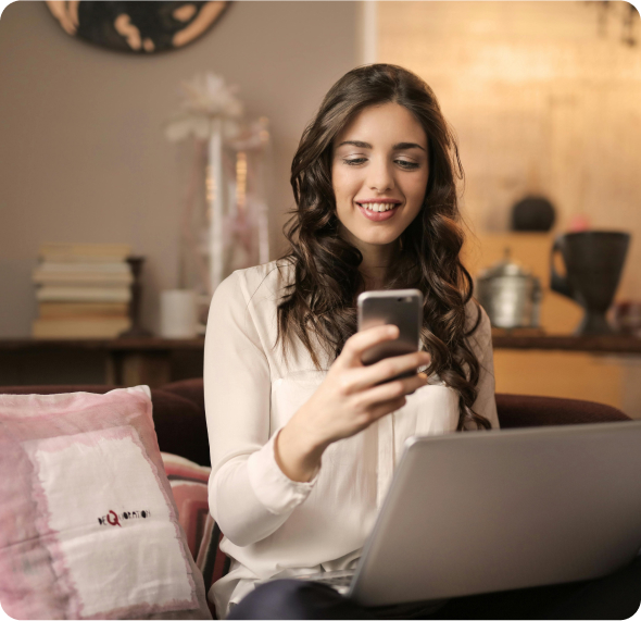 woman checking her phone and smiling while also holding a laptop